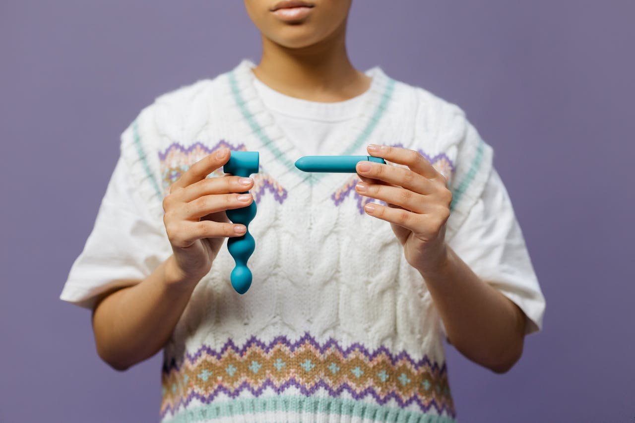 An individual holds two teal adult toys against a purple background, emphasizing modern adult lifestyle.