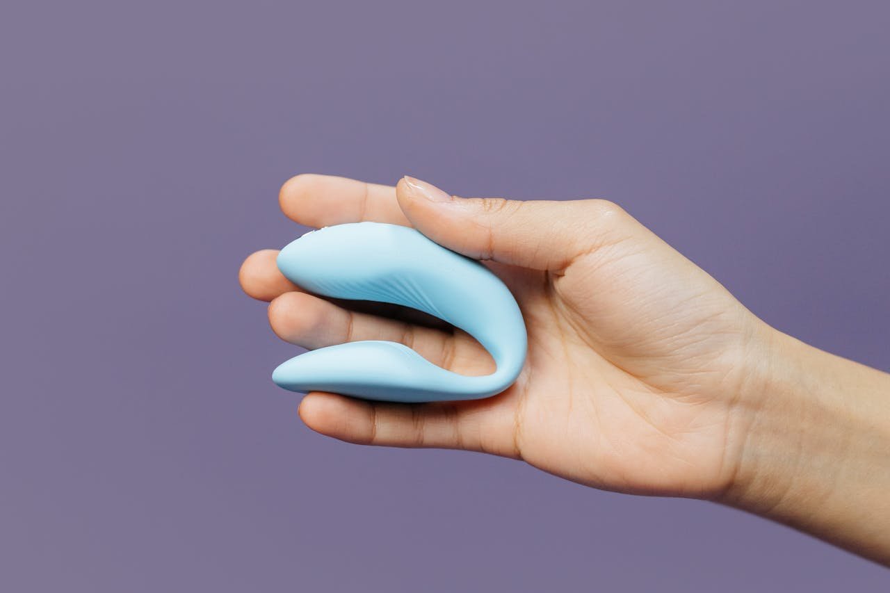 A hand holding a small blue vibrator against a purple background, symbolizing intimacy.