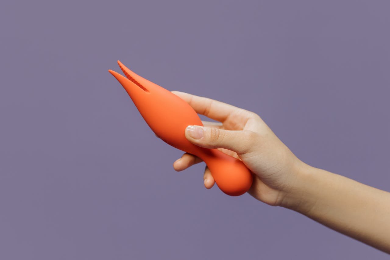 A close-up of a hand holding an orange vibrator against a minimalistic purple backdrop, showcasing modern sensuality.
